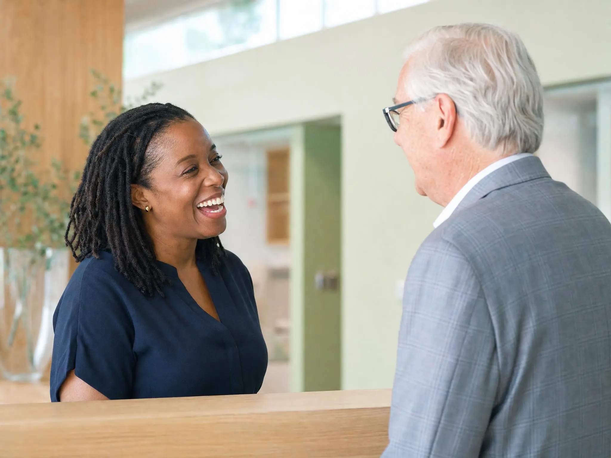 A hospital communications director mid-conversation with a colleague across a reception counter.