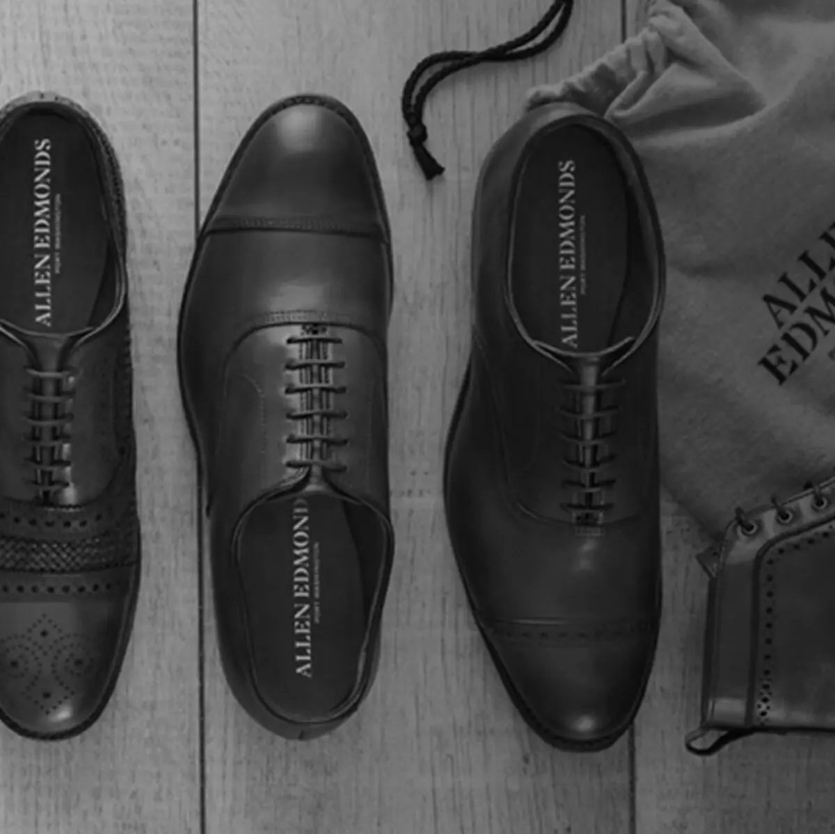 Three pairs of Allen Edmonds leather oxfords laid out on a wooden surface beside a dust bag.