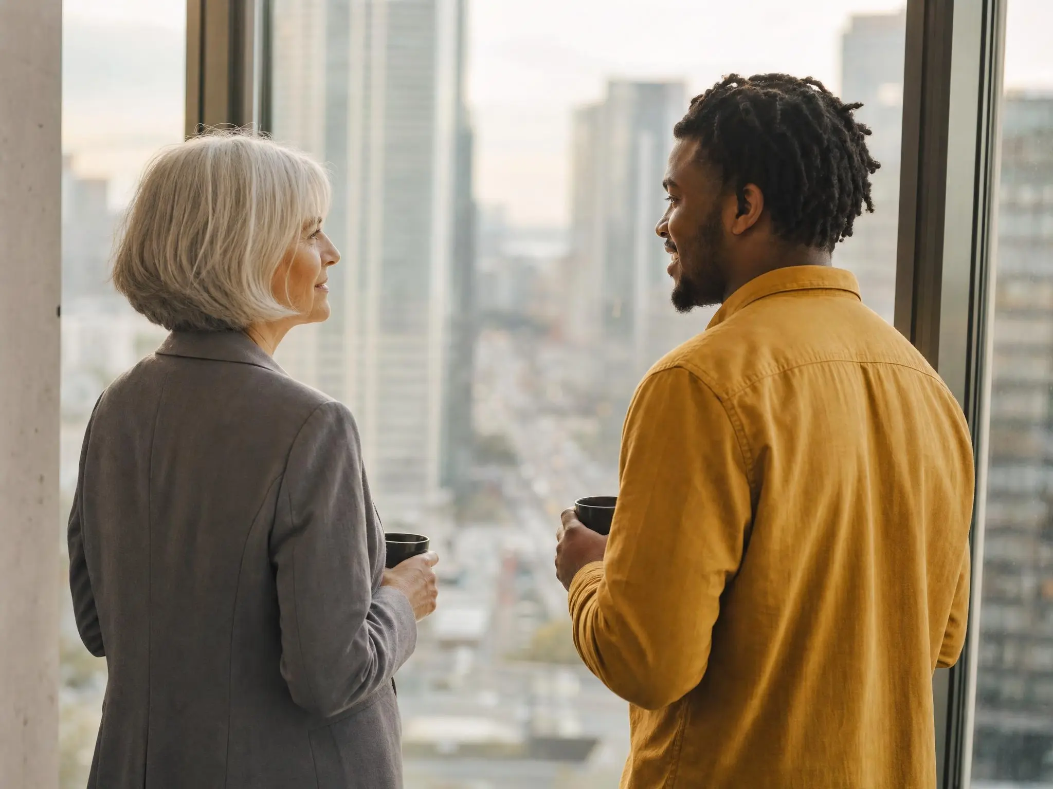 Two colleagues at a window with coffee, talking over which parts of the map their buyer actually lives in.