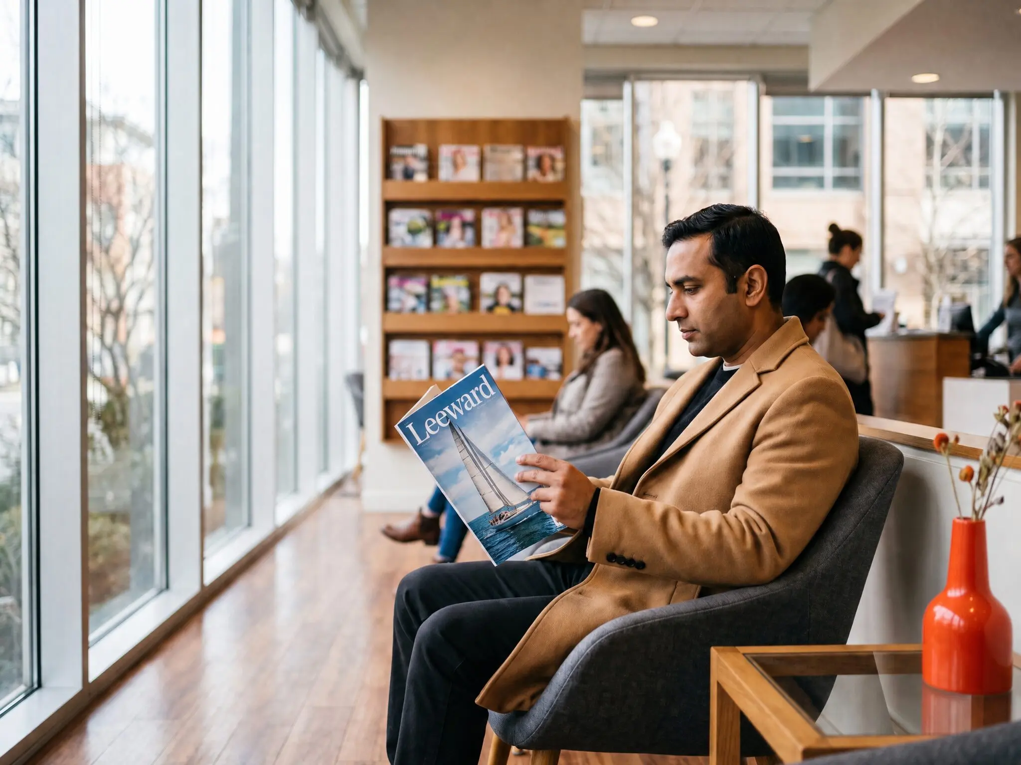 A man in a camel overcoat absorbed in a sailing magazine in a bright optometrist waiting area, a rack of magazines on the wall behind him.